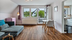 A modern living room with a sofa, dining table, chairs, and a small kitchen area. - Studio Apartment 'Ruhiges Apartment' with Balcony and Wi-Fi (Horn-Bad Meinberg)