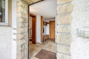 Un couloir aux murs de pierre, avec une porte en bois, un banc et un porte-manteau.