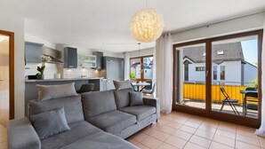 A modern living room with a grey sectional sofa, a dining area with a table and chairs, and a kitchen with grey cabinets. - Apartment 'Seeside' with Lake View, Balcony and Wi-Fi (Uhldingen-Mühlhofen)