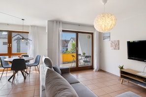 A modern living room with a sofa, dining table, chairs, and a TV.