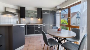 A modern kitchen with grey cabinets, a round dining table with chairs, and a large window with a view of houses. - Apartment 'Seeside' with Lake View, Balcony and Wi-Fi (Uhldingen-Mühlhofen)