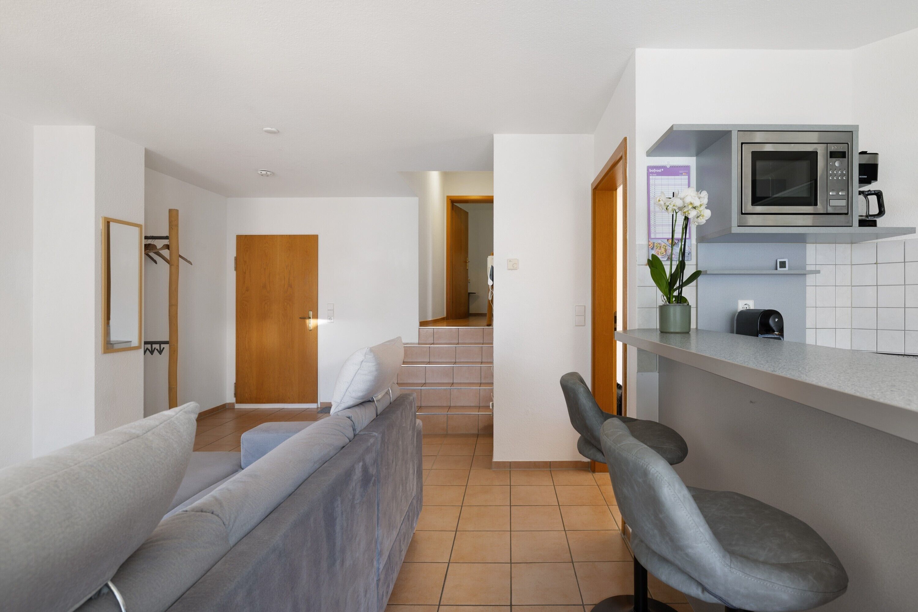Una cocina moderna con microondas, cafetera y una pequeña barra. Se ve una escalera que lleva a otra habitación.