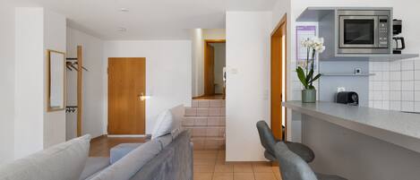 Una cocina moderna con microondas, cafetera y una pequeña barra. Se ve una escalera que lleva a otra habitación.