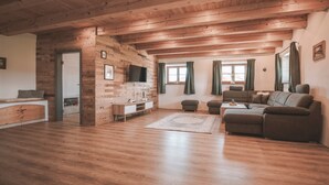 A wooden-floored living room with a sofa, a TV, and a small table. - Holiday Home 'Kaiser' with Mountain View, Private Terrace and Wi-Fi (Aßling)