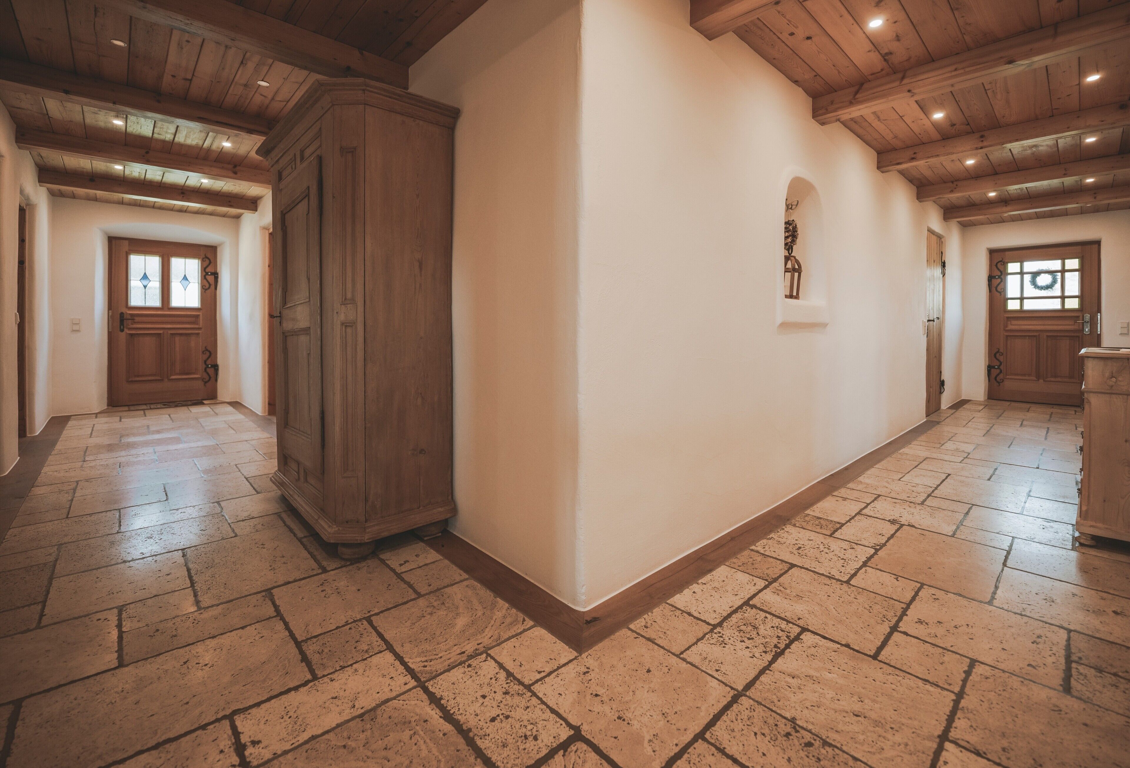 A spacious hallway with wooden floors, white walls, and wooden doors.