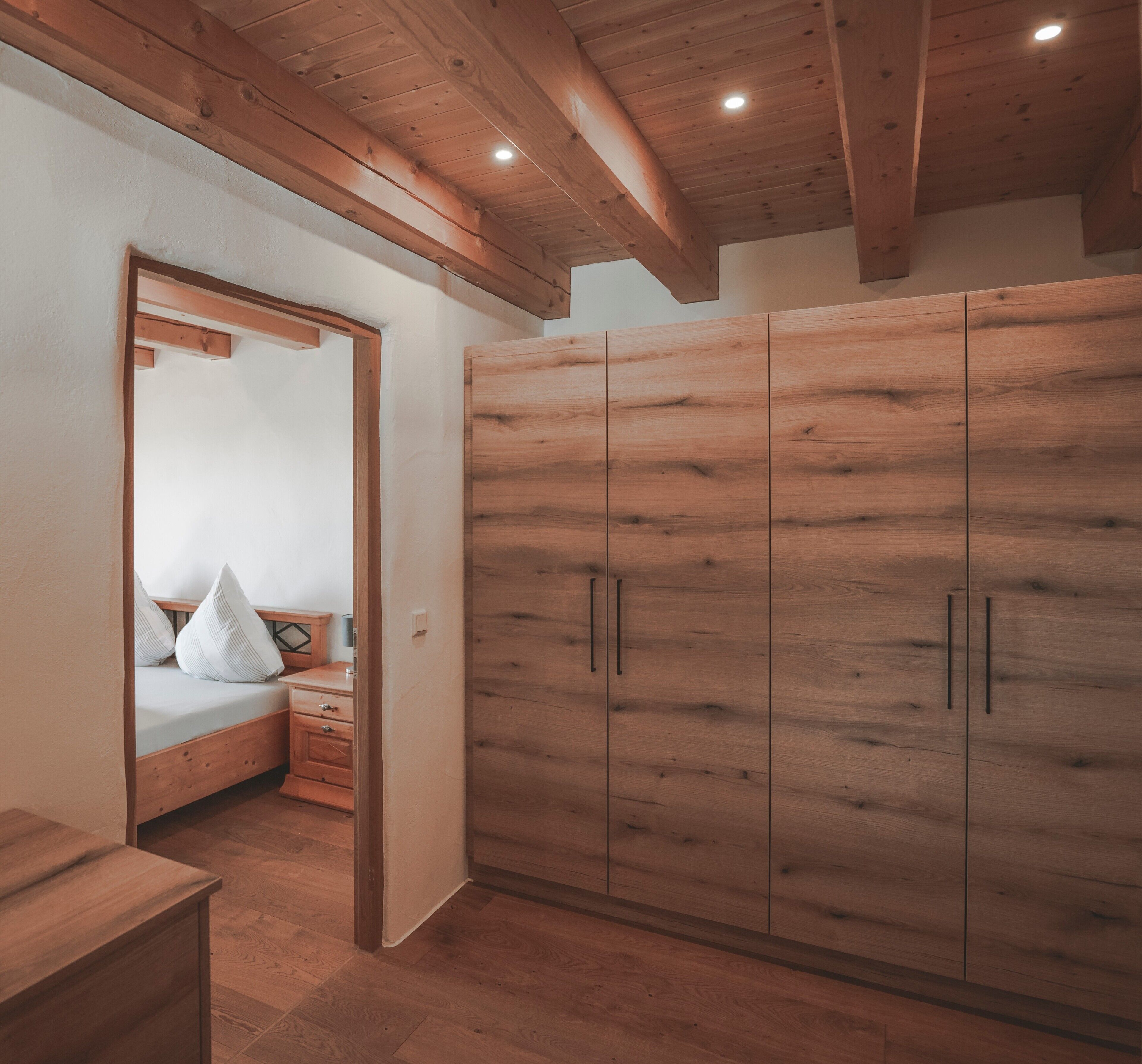 A bedroom with a wooden wardrobe, a bed with pillows, and a wooden dresser.