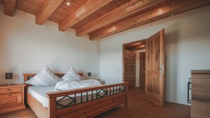 A bedroom with a wooden bed, nightstands, a dresser, and a wooden ceiling. - Holiday Home 'Kaiser' with Mountain View, Private Terrace and Wi-Fi (Aßling)