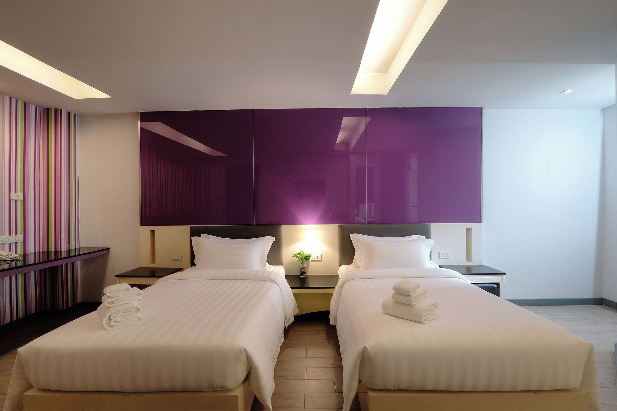 A hotel room with two beds, a large mirror, and a striped curtain.