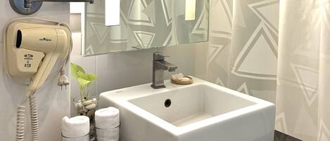 A modern bathroom with a white sink, a round mirror, a hairdryer, and a glass container with toiletries.