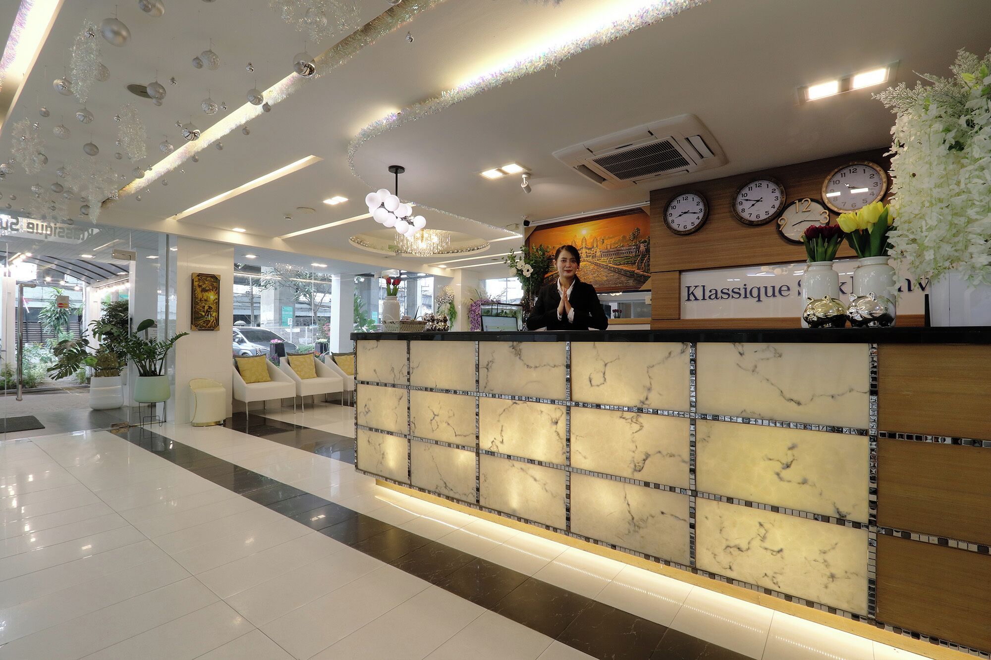 A hotel reception area with a marble reception desk, a chandelier, clocks, and a sign that reads "Klasseque".