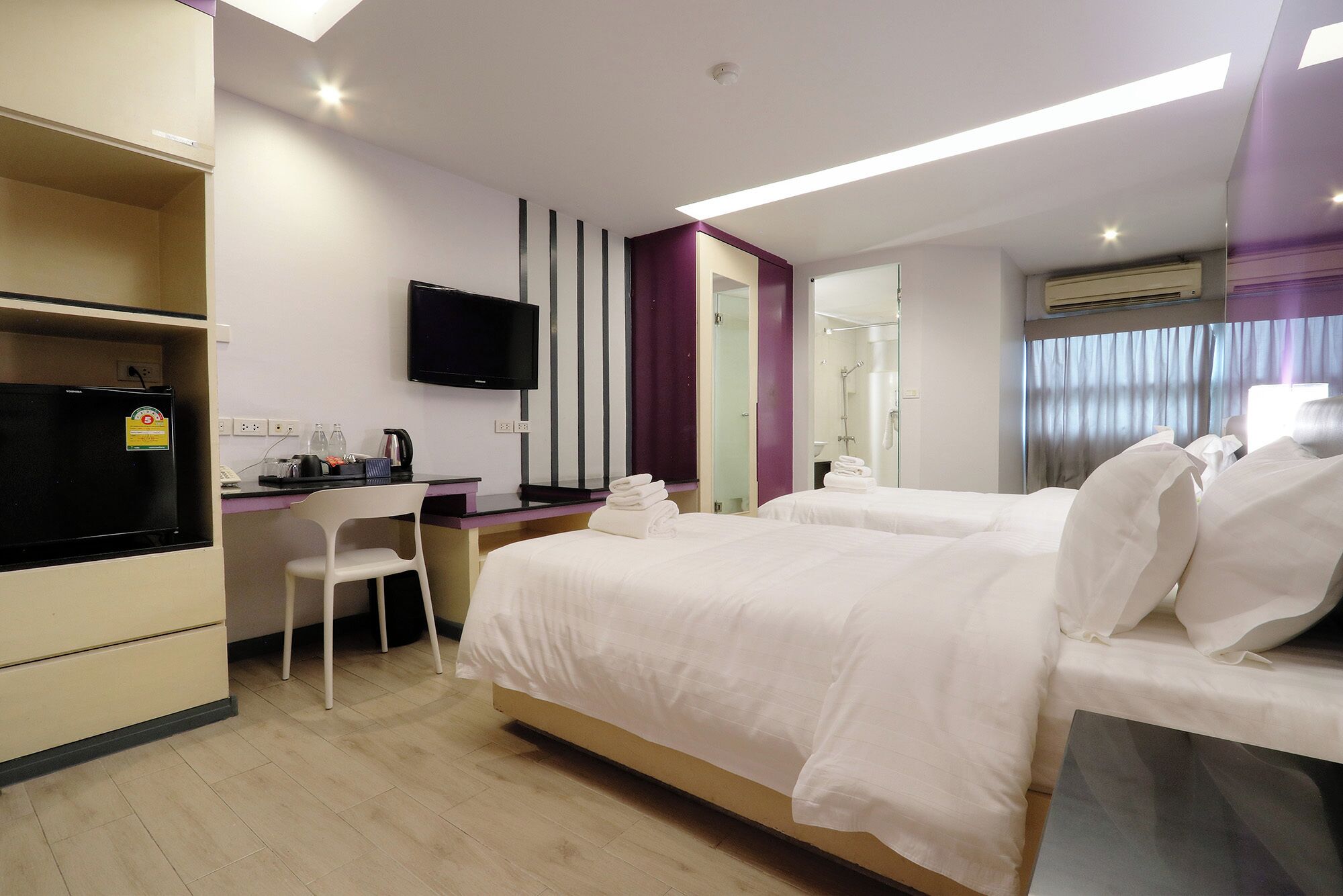 Une chambre d’hôtel avec deux lits, un bureau avec une chaise, une télévision et un espace douche.