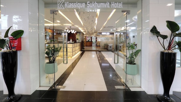 De ingang van het Classic Sukhumvit Hotel, met een receptiebalie, glazen deuren en potplanten.