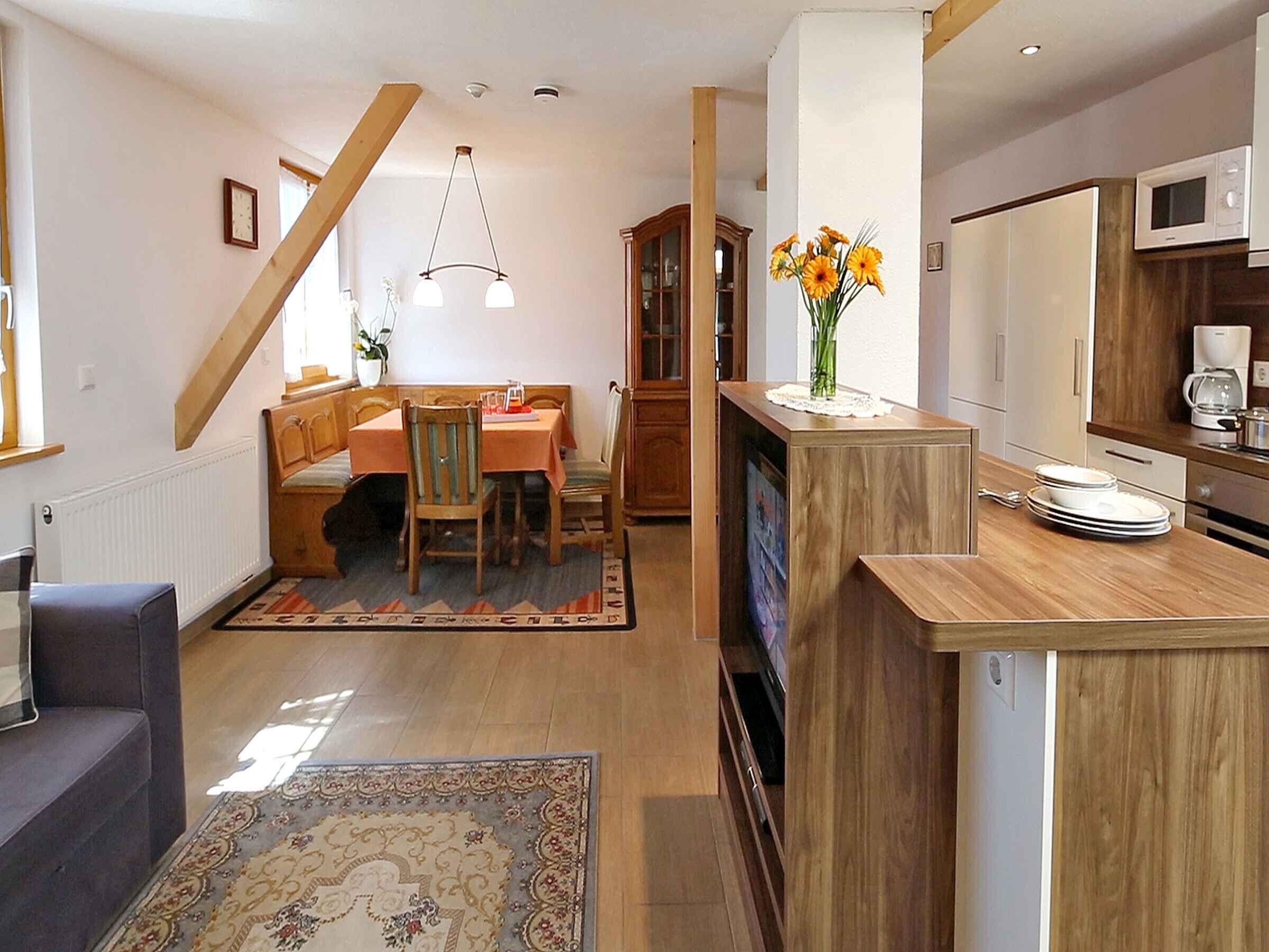 A modern kitchen with wooden cabinets, a dining area with a table and chairs, and a living room with a sofa.