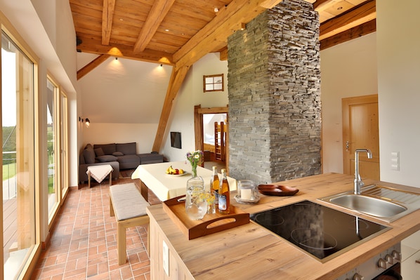 A modern kitchen with a stone column, wooden beams, a large window, and a built-in stove.