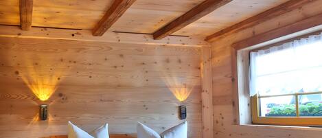 Ein Zimmer einer Holzhütte mit einem Bett, zwei Wandleuchten, einem Fenster und einem Nachttisch.