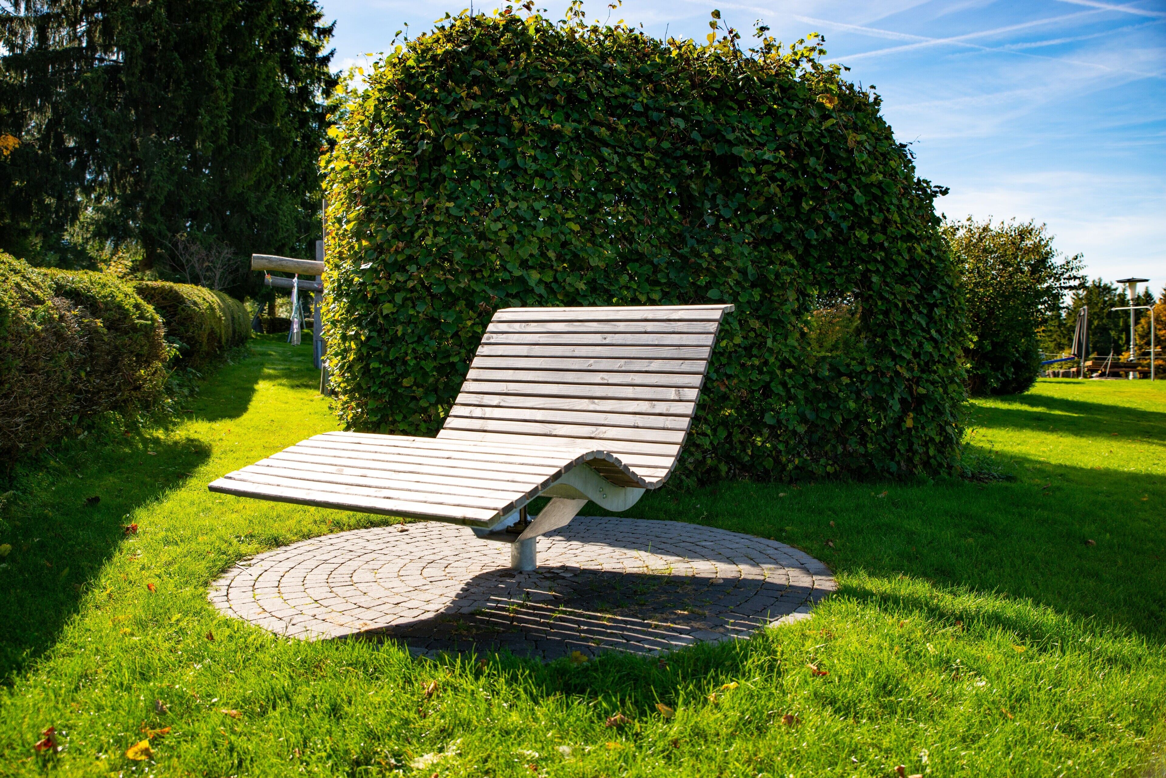 A bench with a curved backrest and a circular base, surrounded by well-maintained grass and a hedge.