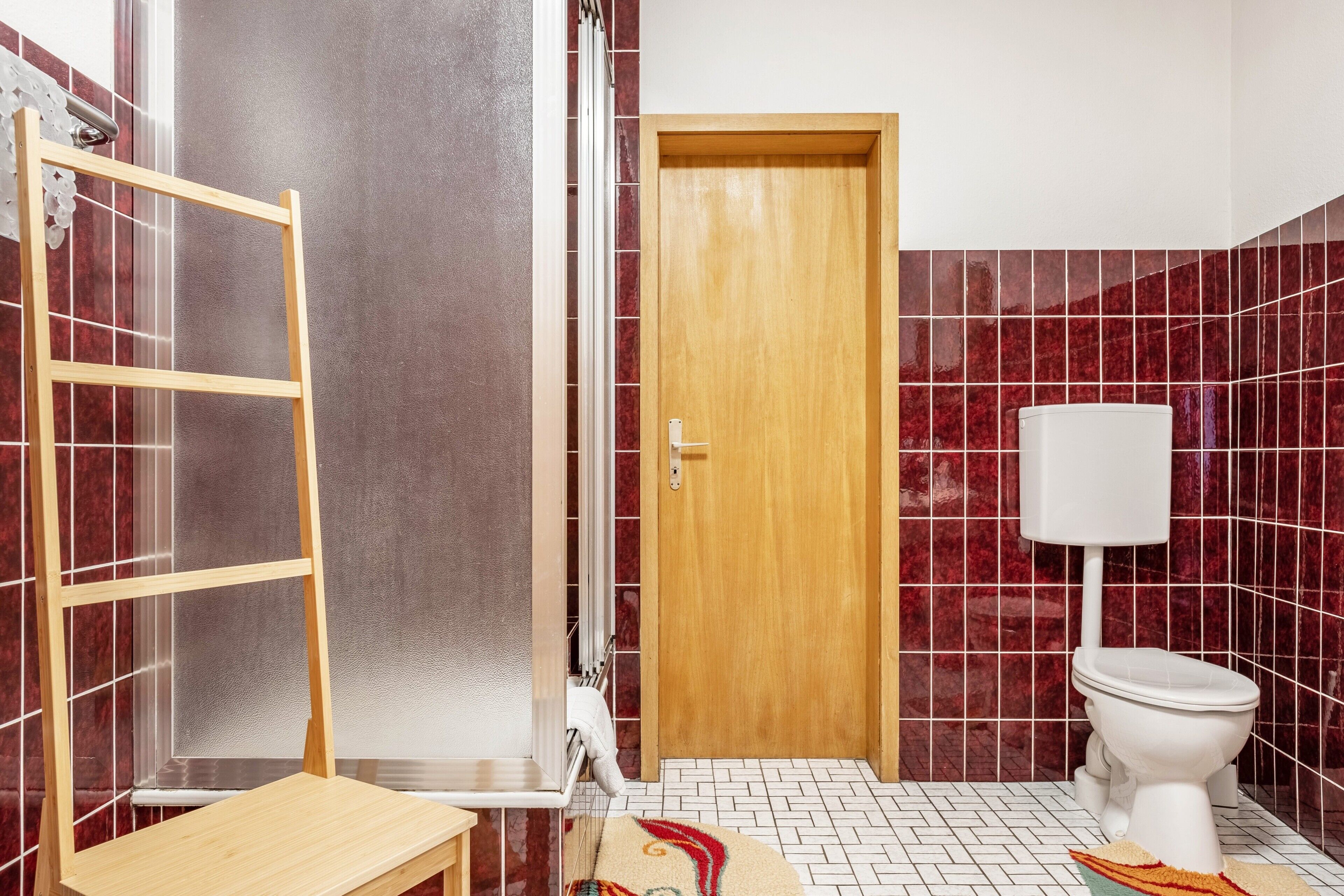 A bathroom with a wooden door, a white toilet, and a shower area with a glass door.