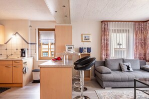 Un salon moderne comprenant un canapé, une table basse, un coin cuisine avec un évier et des placards, ainsi qu’un tabouret de bar.