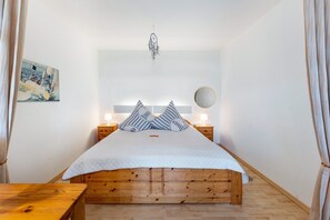Una camera da letto con un letto di legno, due comodini con lampade, un dreamcatcher appeso al muro e un quadro.