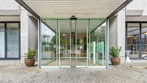 A building entrance with a glass door, potted plants, and a brick-paved ground.