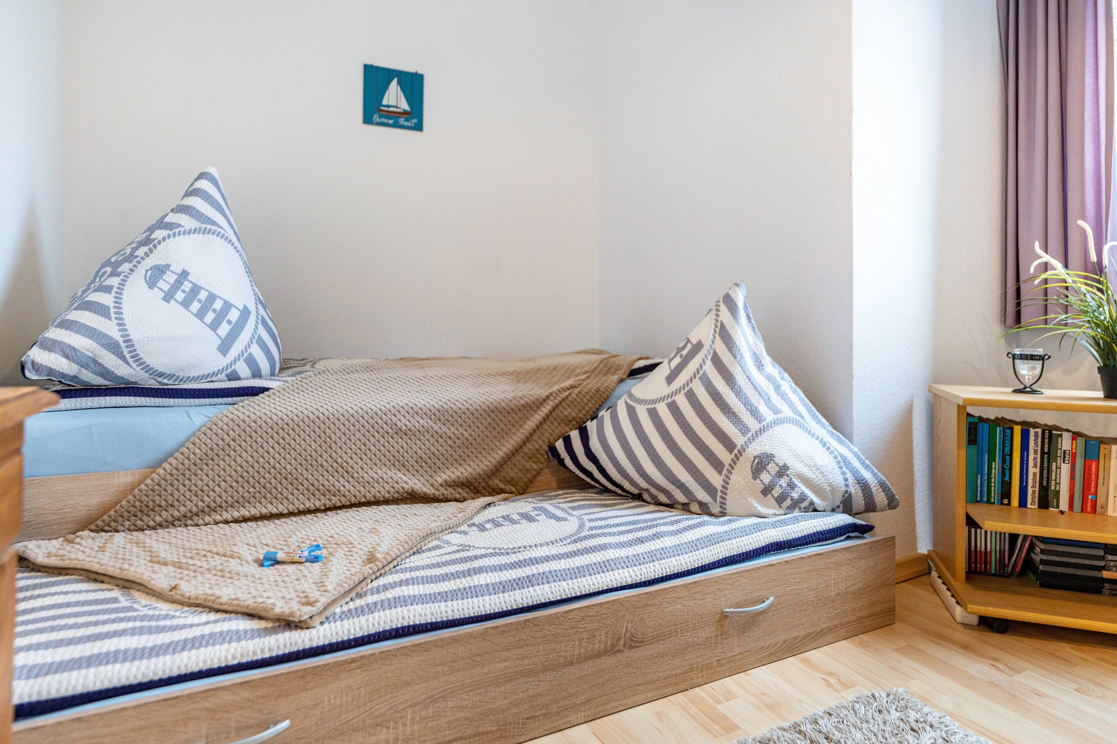 A cozy room with a bed, pillows, a bookshelf, and a small plant.