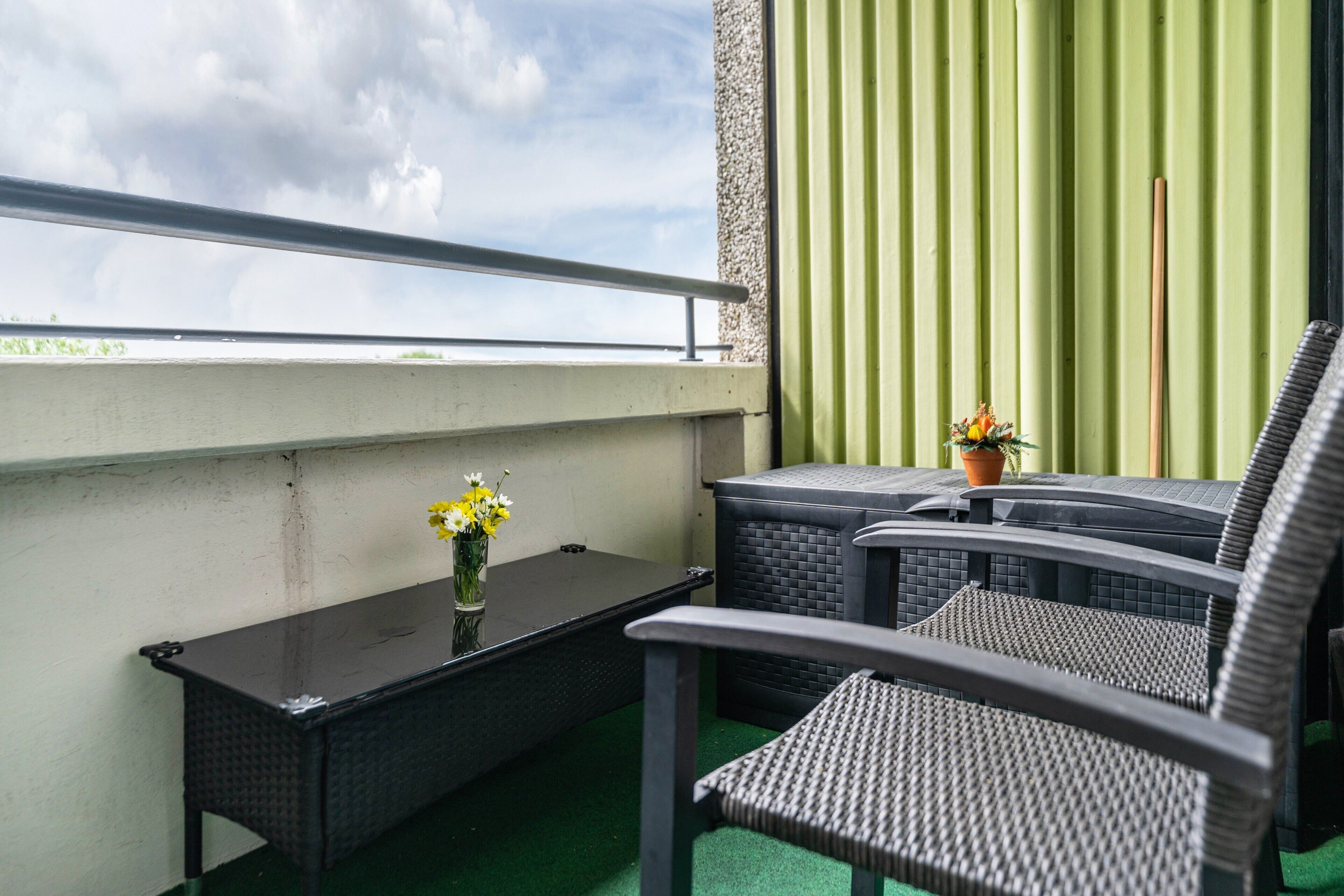 En balkon med et bord, to stole, en potteplante og udsigt til himlen.