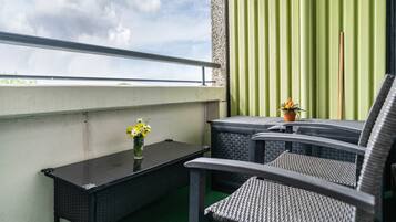 En balkon med et bord, to stole, en potteplante og udsigt til himlen.