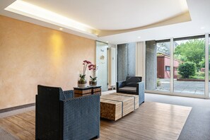 A modern lobby with a reception desk, seating area, and large windows offering a view of the outdoors.