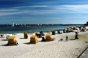 A beach with yellow beach huts, a pier with sailboats, and a clear blue sky. - Holiday Apartment 'Strandperle-Schilksee' with Sea View, Conservatory and Wi-Fi (Kiel)
