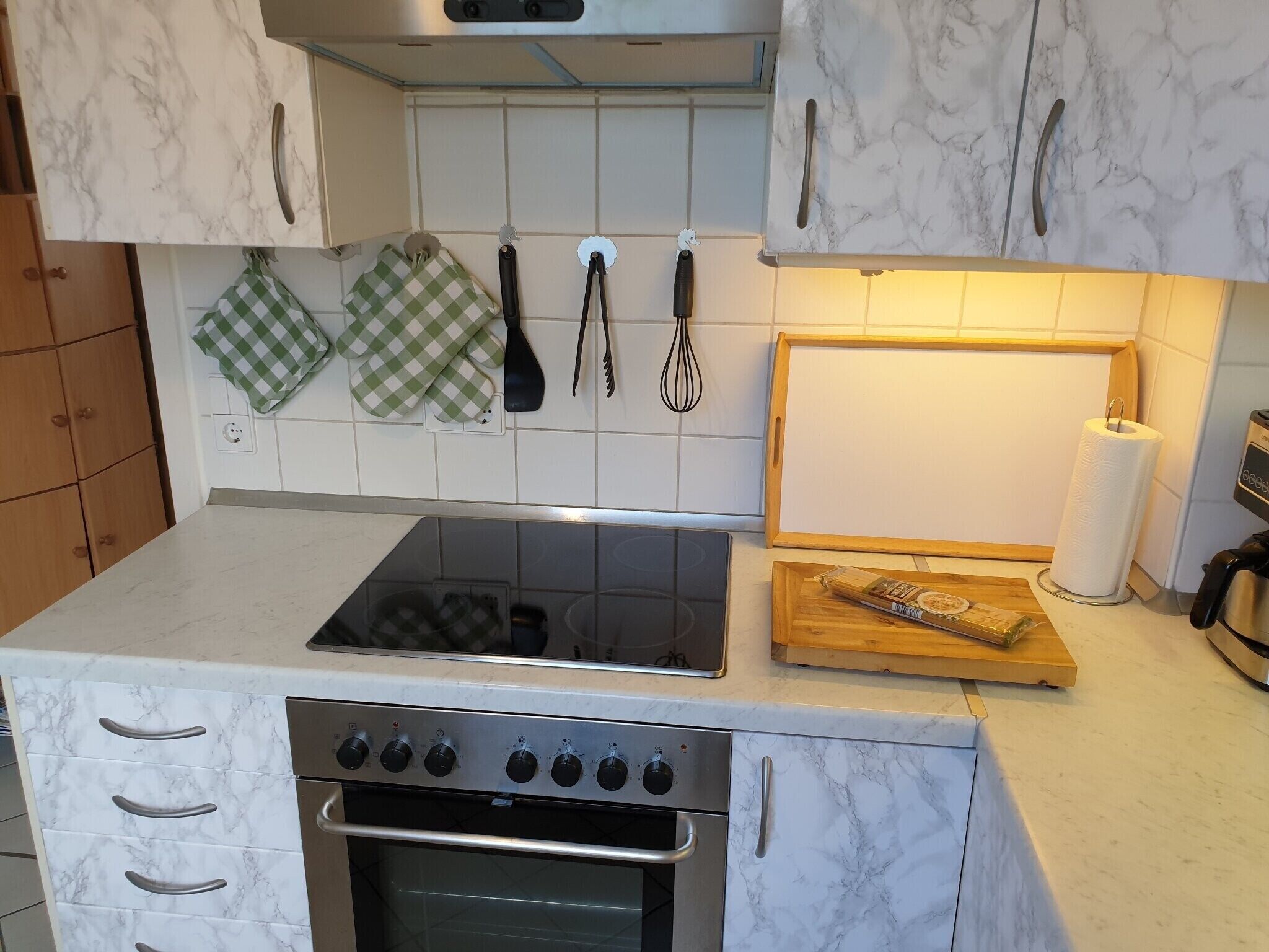 A kitchen with a stove, oven, and a wooden cutting board with a bottle.