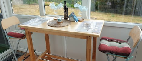 A wooden table with a view of the outdoors, two chairs, and a bottle of wine.