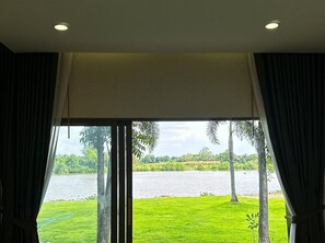 A room with a large window overlooking a lake, curtains, and a ceiling light. - VAA Chachoengsao (Khlong Khuean)