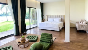 Ein modernes Schlafzimmer mit einem großen Bett, einem grünen Sofa und Blick auf einen Garten durch eine Schiebetür.