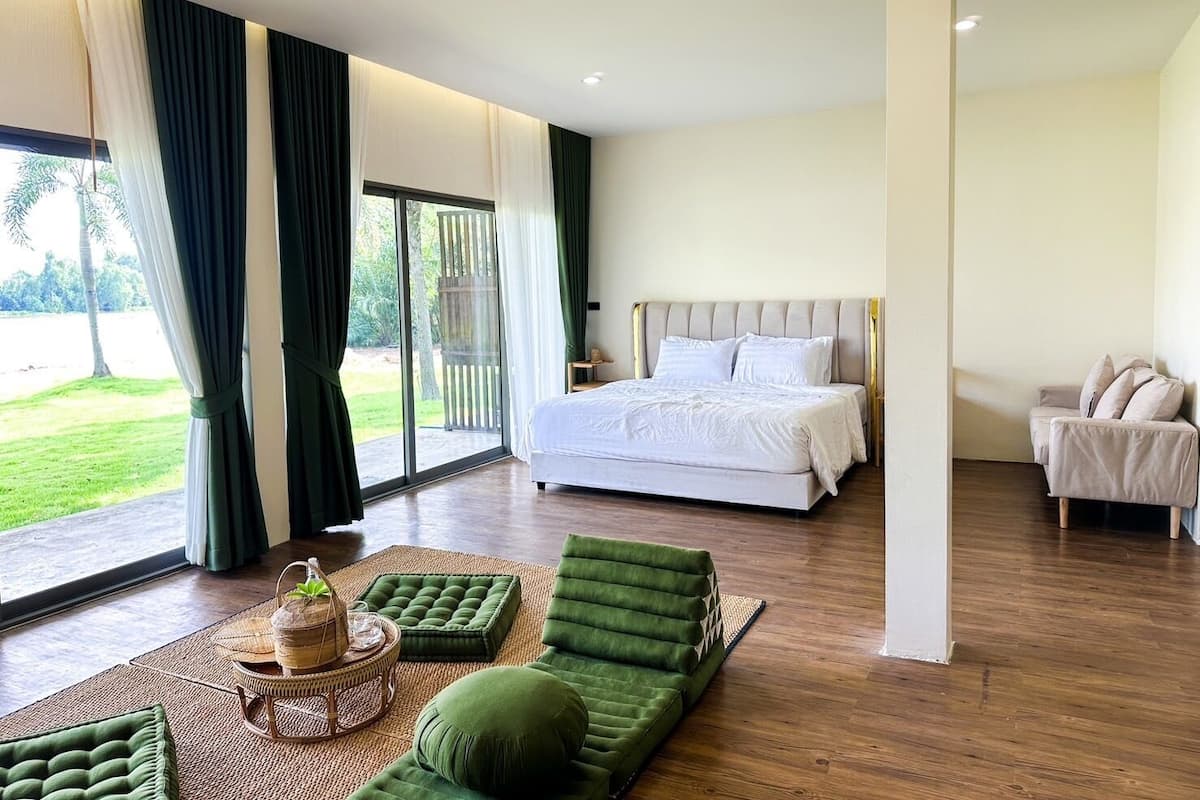 A modern bedroom with a large bed, a green sofa, and a view of a garden through a sliding door.
