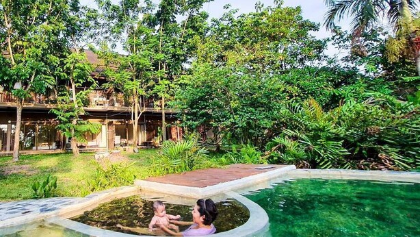 Ein Poolbereich mit klarem Wasser, umgeben von üppiger Vegetation und einer Holzterrasse.