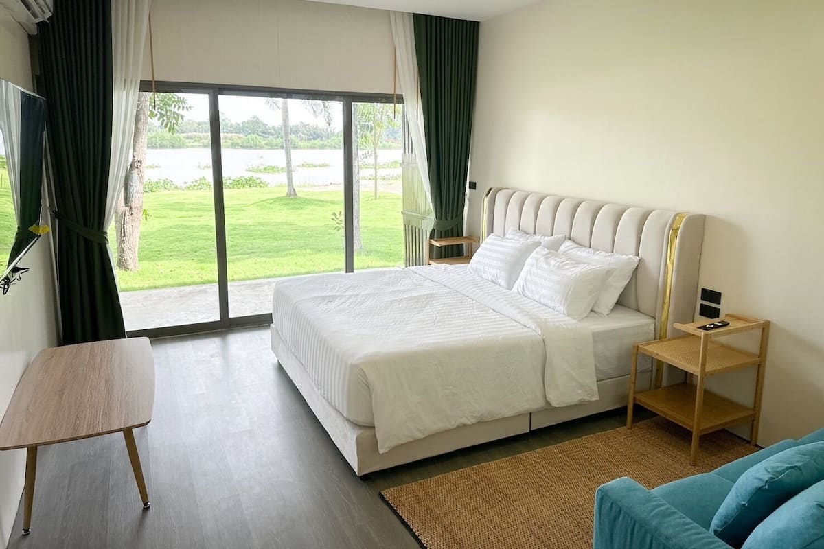 A hotel room with a large bed, a small table, a nightstand, and a view of a green landscape through the window.