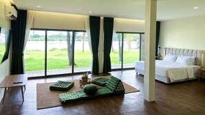Ein geräumiges Schlafzimmer mit einem großen Bett, einem grünen Sofa und Blick auf eine grüne Fläche durch große Fenster.