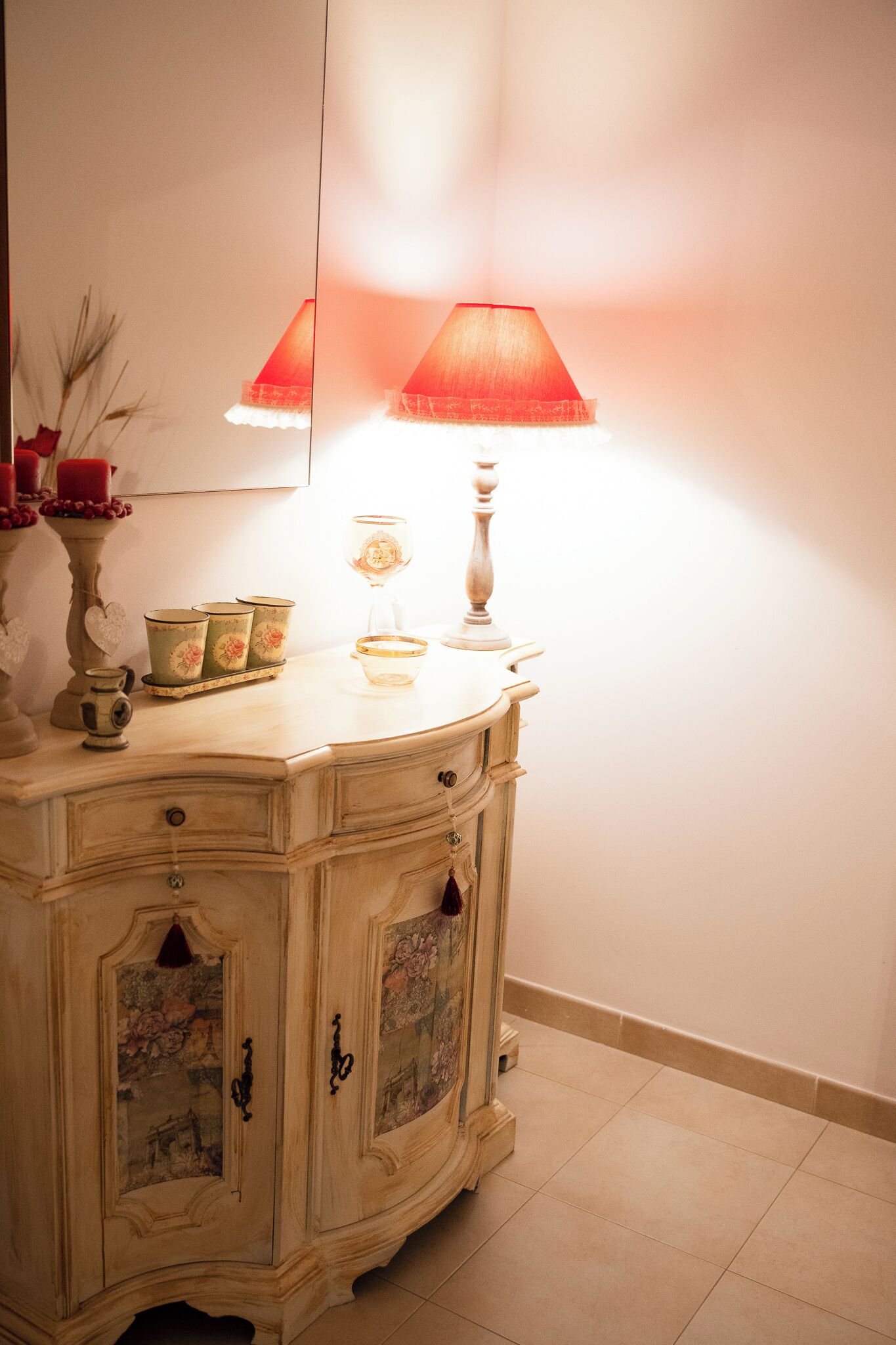Un aparador de estilo antiguo con un espejo encima, una lámpara roja y objetos decorativos sobre el aparador.