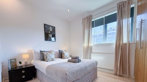 Quarto com cama, mesa de cabeceira, abajur e um quadro na parede.