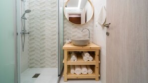 Un bany amb dutxa, un lavabo, un mirall i una estantàcia amb tovalloles.