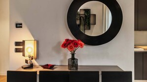 A modern interior with a wall-mounted mirror, a desk with a lamp, and a vase with flowers. - ISIDORO E PERLA FLORENCE SUITES (Firenze)