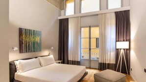 A hotel room with a large bed, a side table, a floor lamp, and a view of the outside balcony through the windows. - ISIDORO E PERLA FLORENCE SUITES (Firenze)