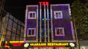 Um edifício com uma placa para 'Vaarahi Restaurant', com letreiros de neon e luzes coloridas.