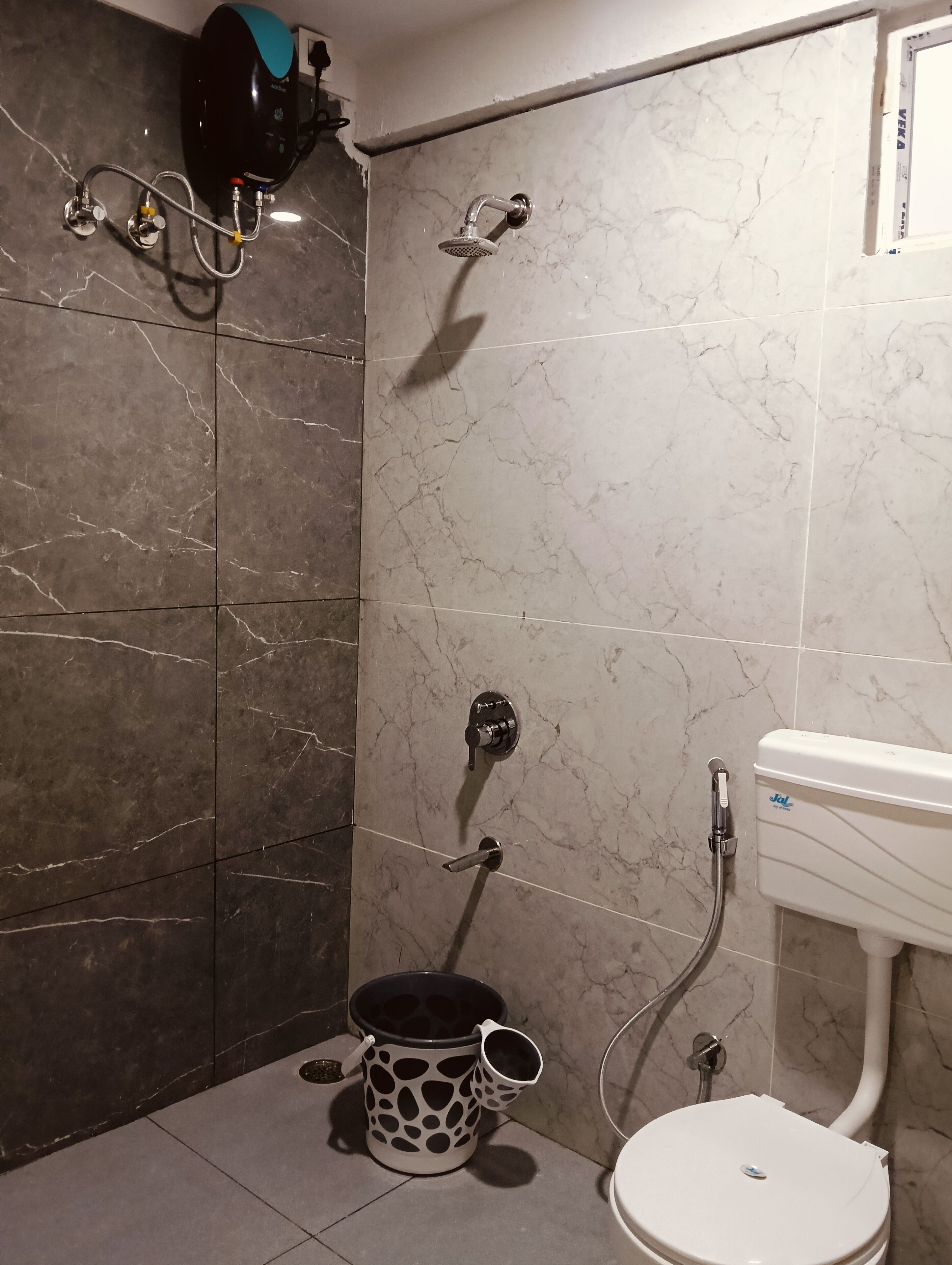 A bathroom with a shower, toilet, and a bucket.