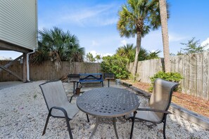 Relax in a tranquil setting with a round table and four chairs surrounded by a gravel ground and lush palm trees.