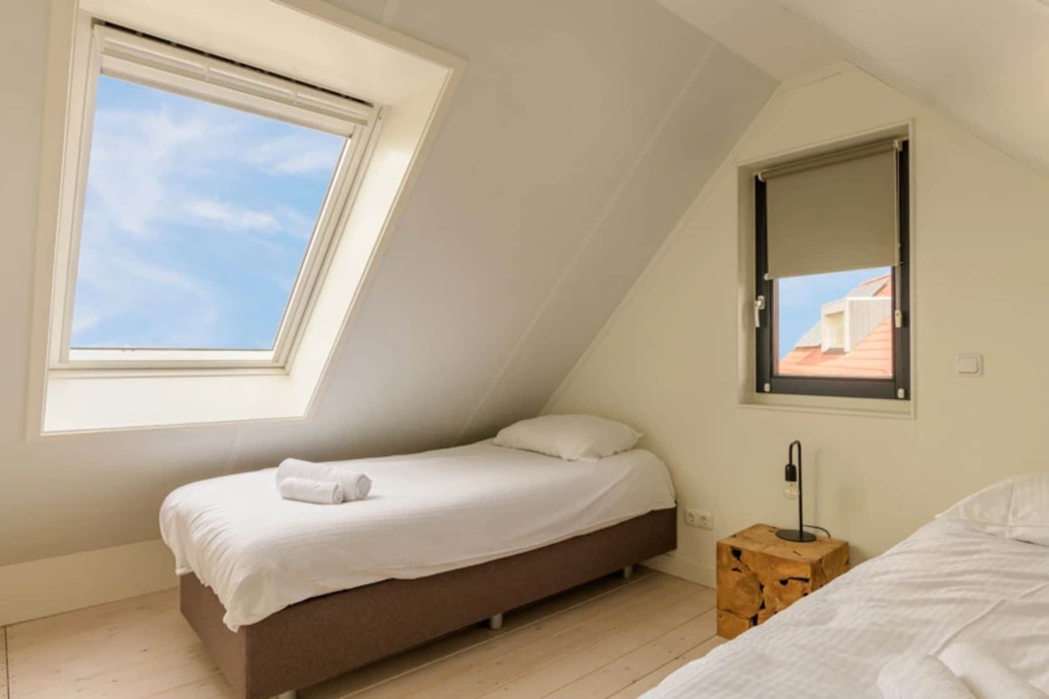 Une petite chambre avec un lit simple, un plafond en pente, un puits de lumière et une fenêtre.
