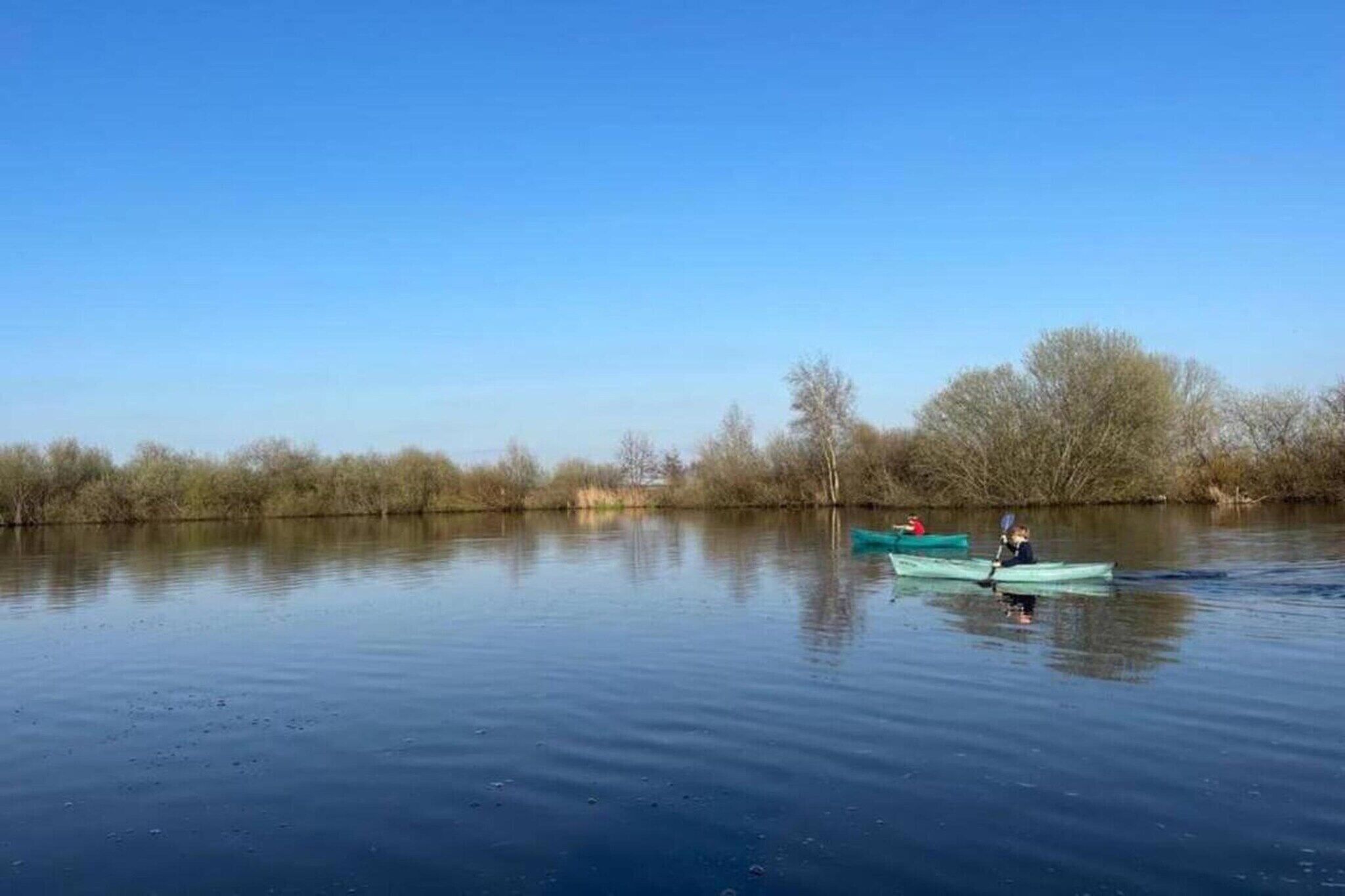 A calm river with two kayaks, one with a person paddling and another stationary.