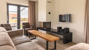 A modern living room with a sofa, a wooden bench, a flat-screen TV, and a fireplace. - Holiday home in Langelille near Lake (Langelille)