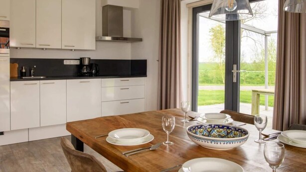 A modern kitchen with white cabinets, a black countertop, and a dining area with a wooden table set for four. - Holiday home in Langelille near Lake (Langelille)