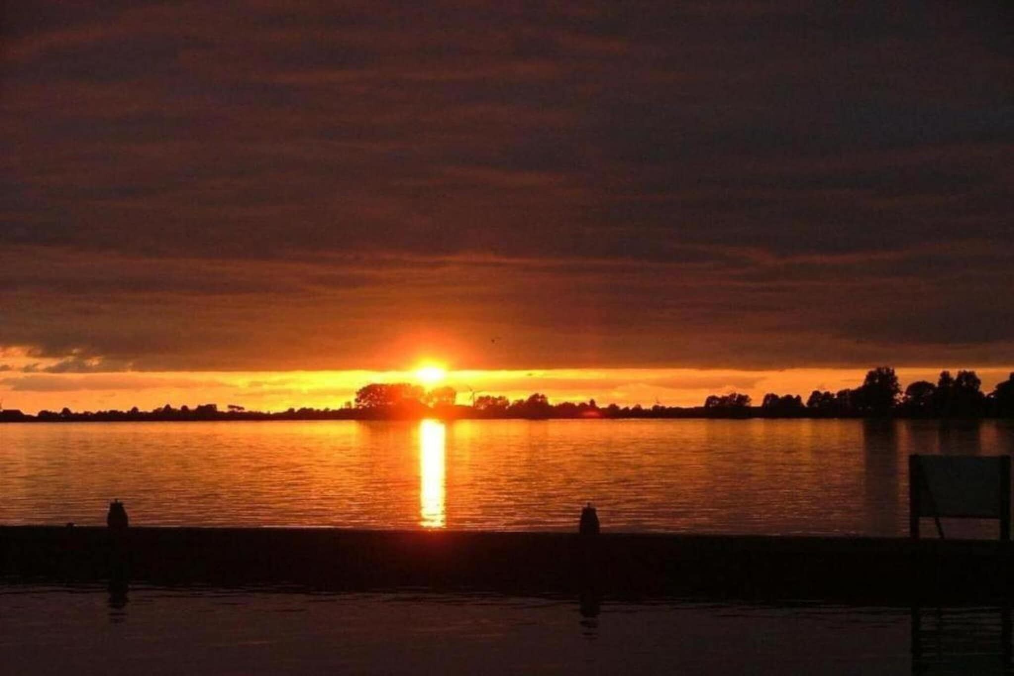 A sunset over a body of water with silhouettes of trees and a chair in the foreground.